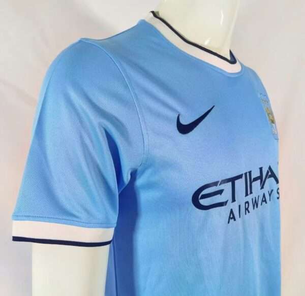 Présente la manche, col et logos du maillot vintage Manchester City Domicile 2013/2014