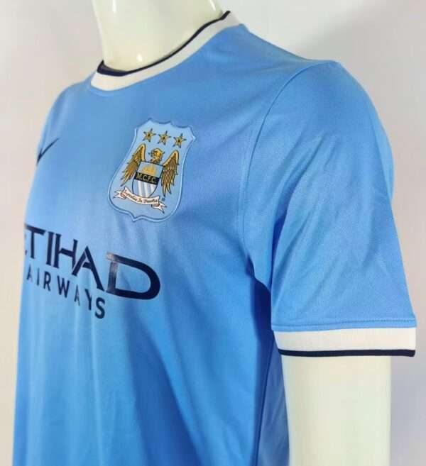 Présente la manche, col et logos du maillot vintage Manchester City Domicile 2013/2014