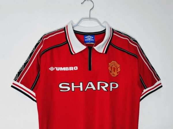 Présente le col, manches et logos du maillot vintage Manchester United Domicile 1998/2000