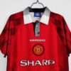 Présente les manches col et logos du maillot vintage Manchester United Domicile 1996/1998