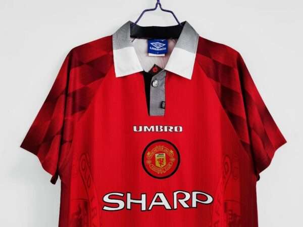 Présente les manches col et logos du maillot vintage Manchester United Domicile 1996/1998